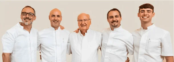 Cinque uomini in camicia bianca sono affiancati e sorridono all'obiettivo su uno sfondo chiaro. Sembrano amichevoli e uniti, rappresentando lo spirito di squadra di Brauner Coppedè Medical Hub di Roma.