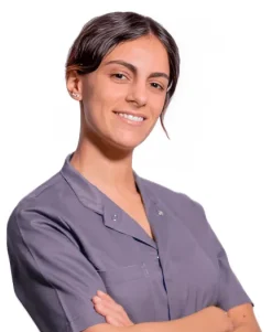 La Dott.ssa Giulia Amelina del Coppedè Medical Hub di Roma, una donna dai capelli scuri in camicia grigia, sta in piedi con le braccia incrociate, sorridendo con sicurezza su uno sfondo bianco.
