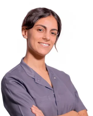 La Dott.ssa Giulia Amelina del Coppedè Medical Hub di Roma, una donna dai capelli scuri in camicia grigia, sta in piedi con le braccia incrociate, sorridendo con sicurezza su uno sfondo bianco.