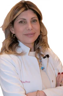 La Dott.ssa Valentina Prece del Coppedè Medical Hub di Roma, una donna dai capelli biondi lunghi fino alle spalle con un camice bianco, si erge sicura di sé con le braccia incrociate e un caldo sorriso su un semplice sfondo bianco.
