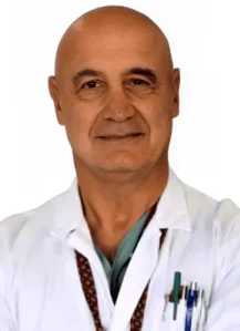 Prof. Valentino Valentini - Coppedè Medical Hub di Roma, un uomo di mezza età con la testa calva, in piedi con le braccia incrociate, camice bianco e stetoscopio, penne in tasca, su uno sfondo bianco.