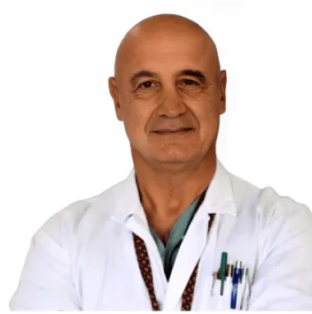 Prof. Valentino Valentini - Coppedè Medical Hub di Roma, un uomo di mezza età con la testa calva, in piedi con le braccia incrociate, camice bianco e stetoscopio, penne in tasca, su uno sfondo bianco.