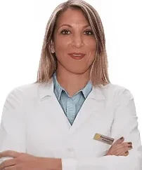 Una donna con lunghi capelli biondi che indossa un camice bianco e un colletto blu sta in piedi con le braccia incrociate e sorride alla telecamera su uno sfondo bianco al Sayaka Papaluca Coppedè Medical Hub di Roma.