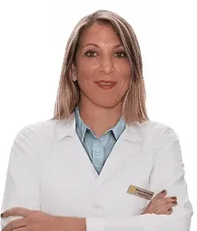 Una donna con lunghi capelli biondi che indossa un camice bianco e un colletto blu sta in piedi con le braccia incrociate e sorride alla telecamera su uno sfondo bianco al Sayaka Papaluca Coppedè Medical Hub di Roma.