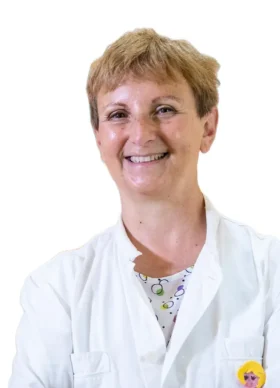 La Prof.ssa Maria Teresa Fadda, una persona sorridente con i capelli corti, indossa un camice bianco e una camicia a fantasia, in posa su uno sfondo bianco semplice.